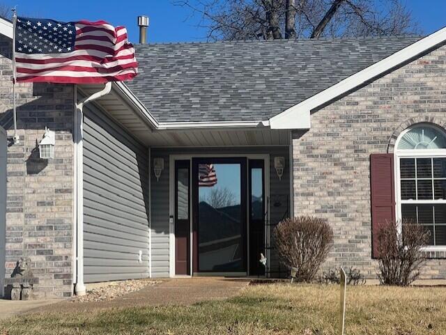 entrance to property featuring brick siding and a shingled roof