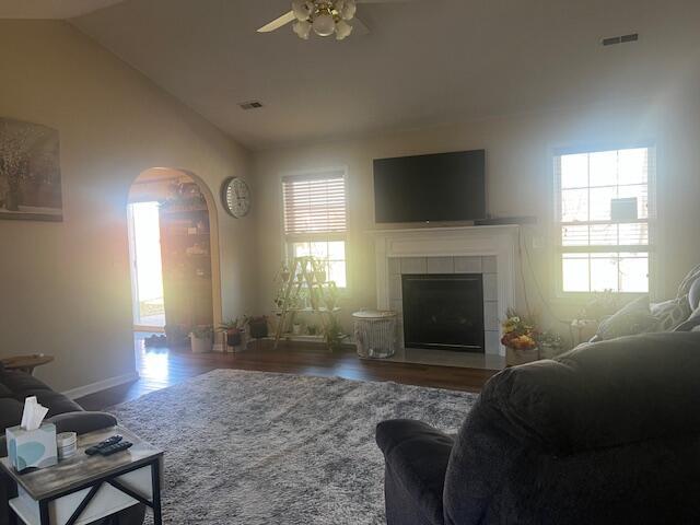 living area featuring visible vents, vaulted ceiling, a tiled fireplace, and wood finished floors