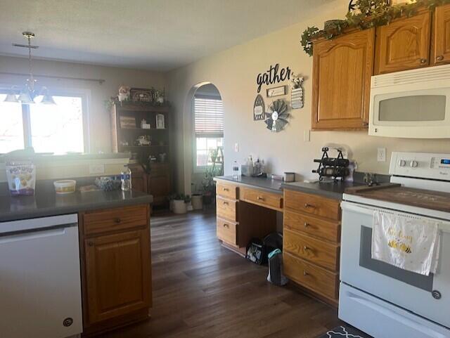 kitchen featuring white appliances, dark wood-type flooring, dark countertops, and brown cabinetry