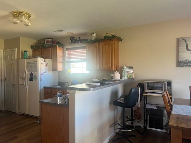 kitchen featuring a breakfast bar, white refrigerator with ice dispenser, dark countertops, dark wood-type flooring, and a peninsula