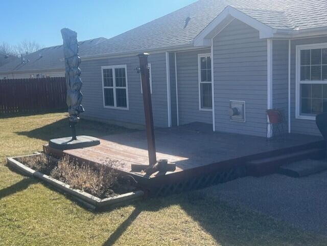 rear view of house with a shingled roof, fence, a deck, and a lawn