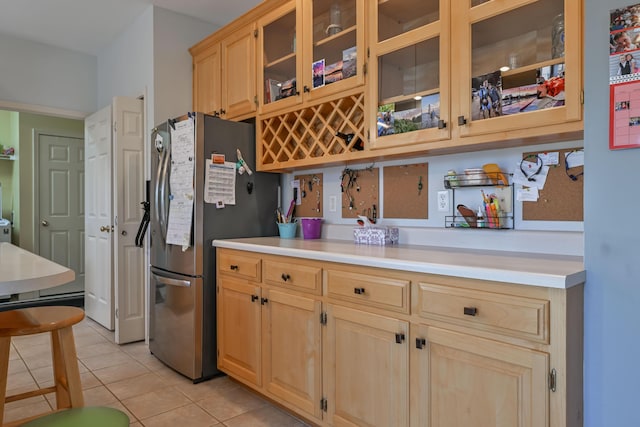 kitchen featuring light countertops, freestanding refrigerator, light tile patterned floors, and light brown cabinetry