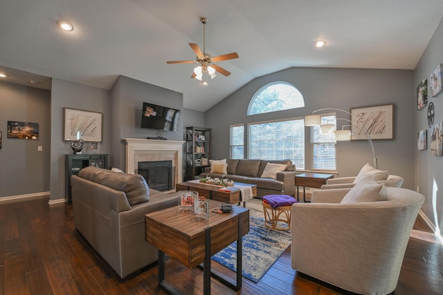 living area with dark wood-type flooring, a fireplace, a ceiling fan, baseboards, and vaulted ceiling