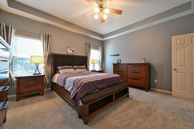 carpeted bedroom with a ceiling fan, multiple windows, baseboards, and a tray ceiling