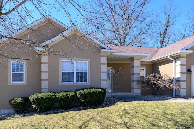 view of front of home featuring roof with shingles, a front yard, and stucco siding