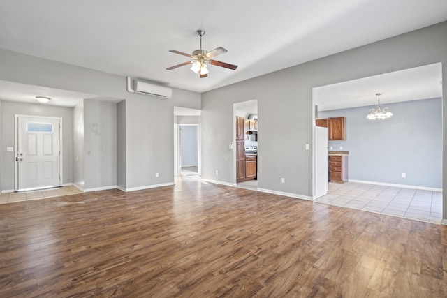 unfurnished living room featuring baseboards, ceiling fan with notable chandelier, wood finished floors, and a wall mounted air conditioner