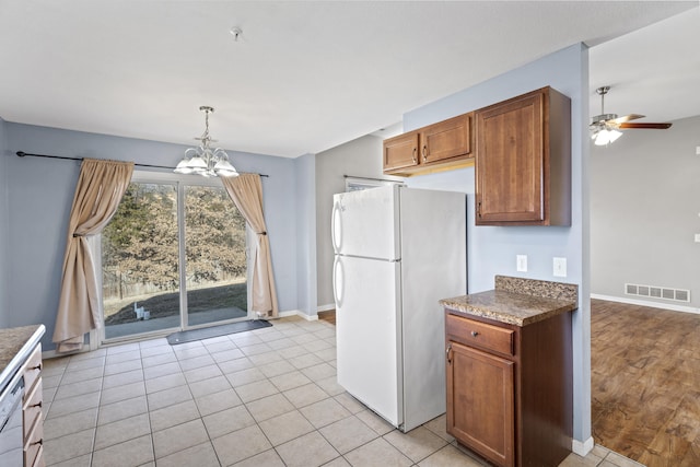 kitchen with brown cabinets, visible vents, freestanding refrigerator, baseboards, and ceiling fan with notable chandelier