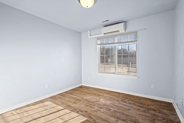 unfurnished room featuring an AC wall unit, wood finished floors, visible vents, and baseboards