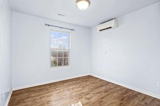 spare room featuring an AC wall unit, wood finished floors, visible vents, and baseboards