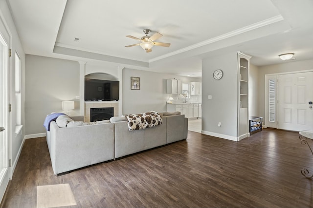 living room featuring dark wood-style floors, baseboards, a raised ceiling, and a tile fireplace