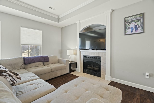 living room featuring crown molding, a raised ceiling, a tiled fireplace, wood finished floors, and baseboards