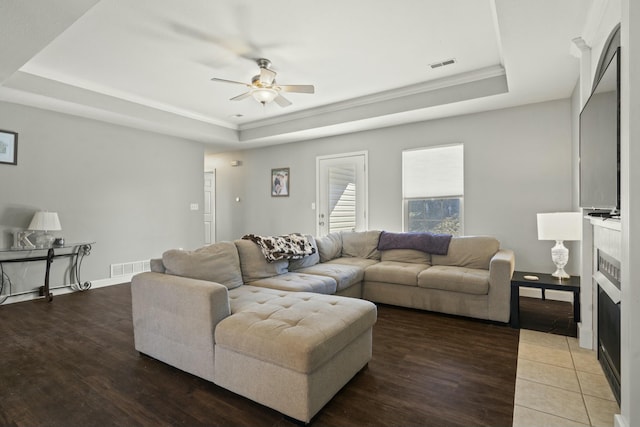 living room featuring light wood-style floors, visible vents, a tray ceiling, and a fireplace with flush hearth