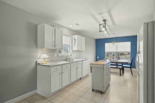 kitchen with light countertops, white cabinetry, a kitchen island, a sink, and white appliances