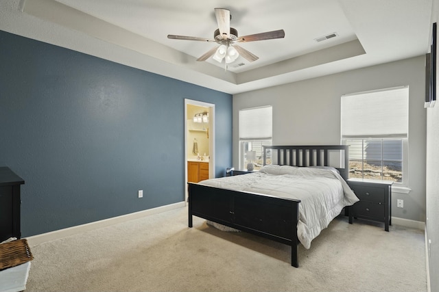 carpeted bedroom featuring baseboards, visible vents, a raised ceiling, a ceiling fan, and ensuite bathroom