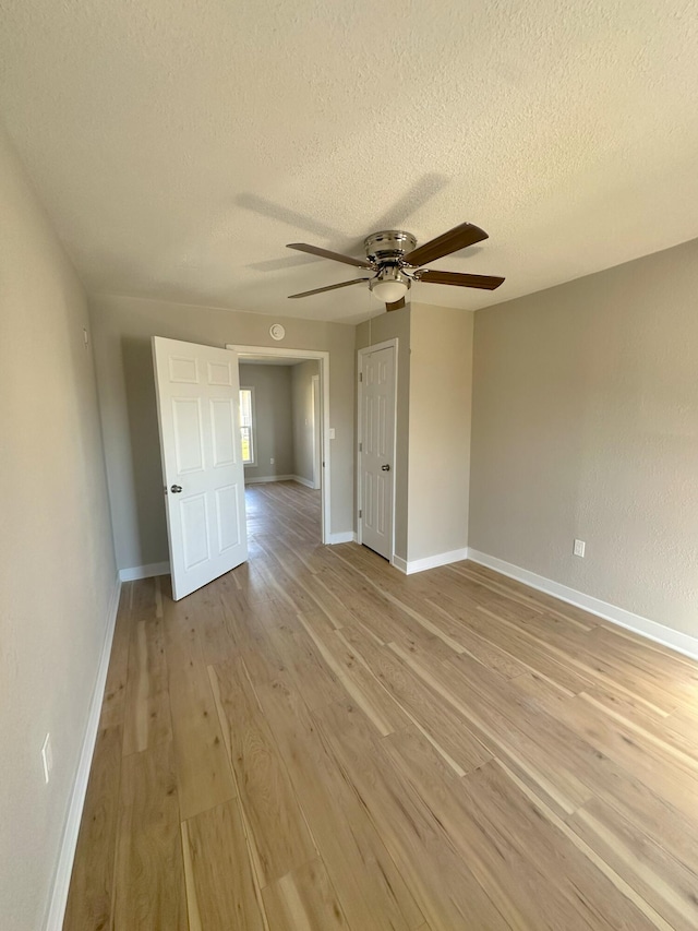 unfurnished room with a textured ceiling, ceiling fan, light wood-type flooring, and baseboards