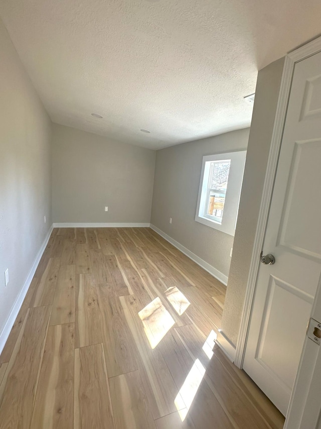 unfurnished room with light wood-style floors, a textured ceiling, and baseboards