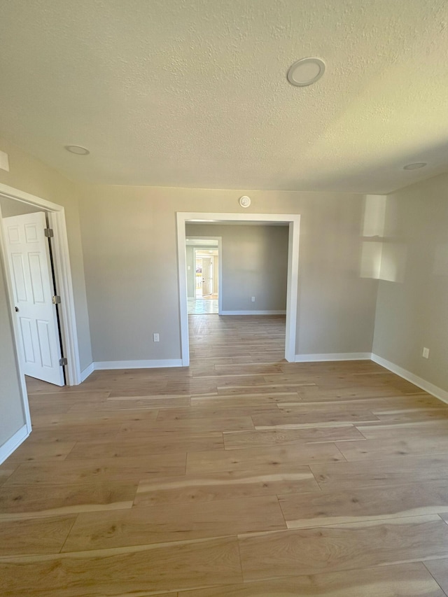 unfurnished room with light wood-style flooring, baseboards, and a textured ceiling