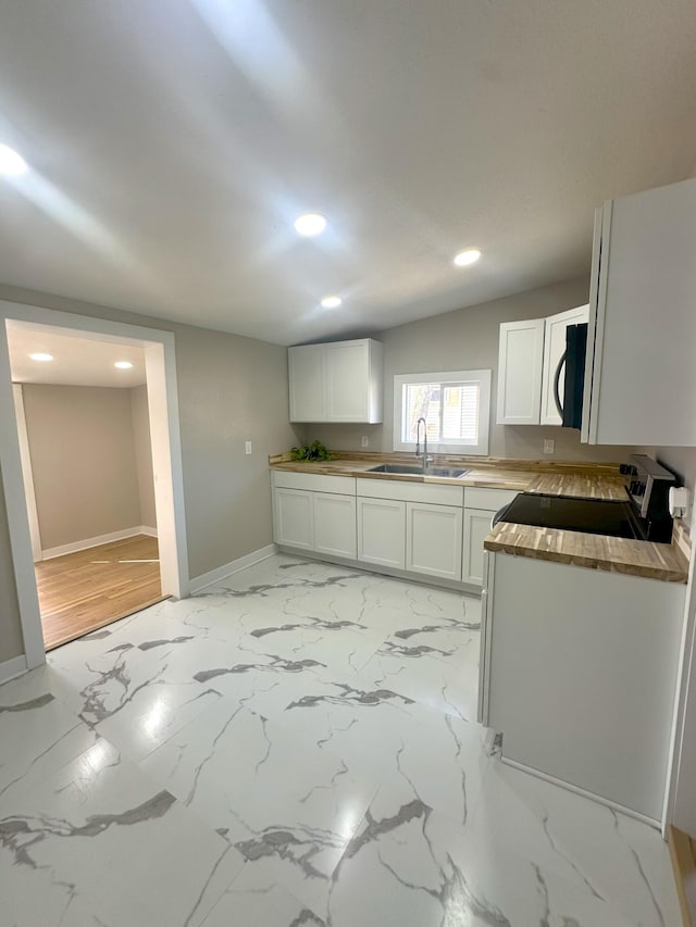 kitchen with recessed lighting, white cabinetry, a sink, black microwave, and baseboards