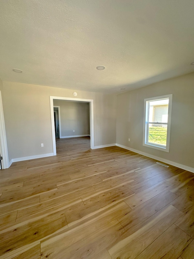 spare room with light wood-type flooring, baseboards, and a textured ceiling