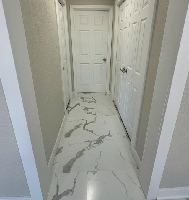 hallway featuring marble finish floor and baseboards