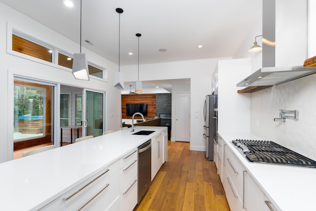 kitchen with appliances with stainless steel finishes, white cabinets, a sink, and wall chimney range hood