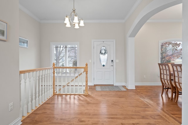 foyer with ornamental molding, arched walkways, a notable chandelier, and wood finished floors