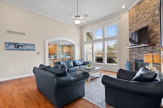 living room featuring arched walkways, a fireplace, visible vents, wood finished floors, and baseboards