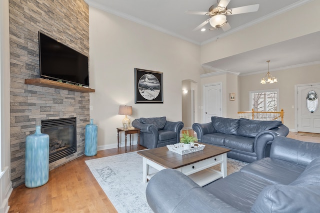 living area with baseboards, arched walkways, ornamental molding, wood finished floors, and a fireplace