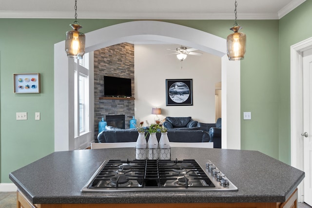 kitchen with a fireplace, dark countertops, stainless steel gas stovetop, ornamental molding, and open floor plan