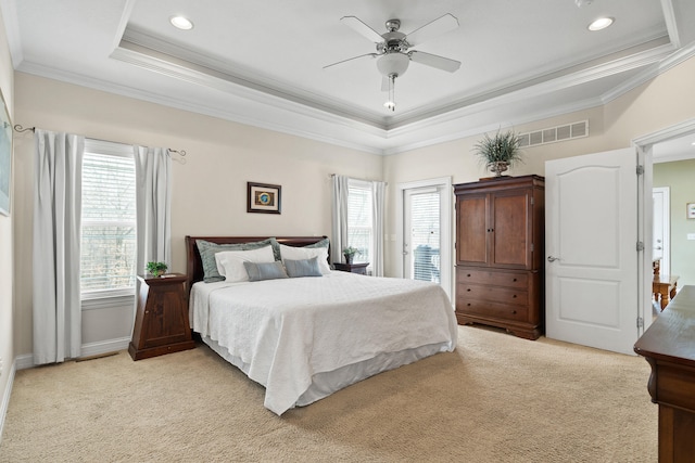 bedroom with a tray ceiling, visible vents, ornamental molding, a ceiling fan, and light carpet