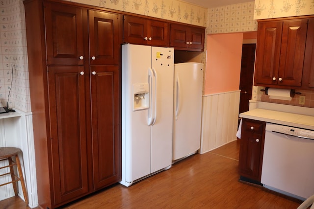 kitchen featuring white appliances, light wood finished floors, wallpapered walls, light countertops, and wainscoting