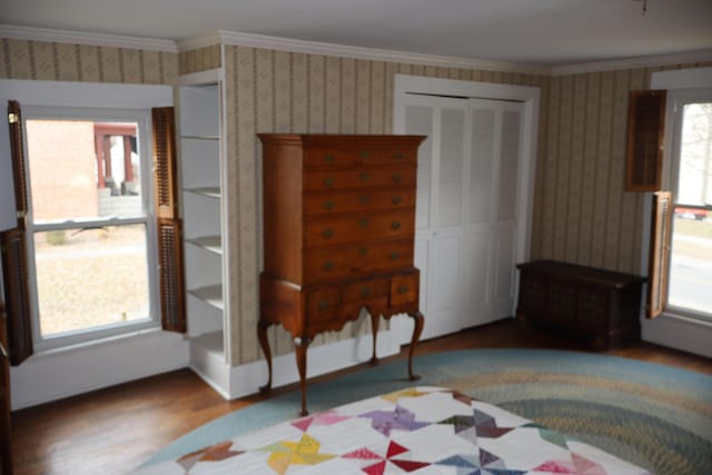 unfurnished bedroom featuring a closet, wood finished floors, crown molding, and wallpapered walls