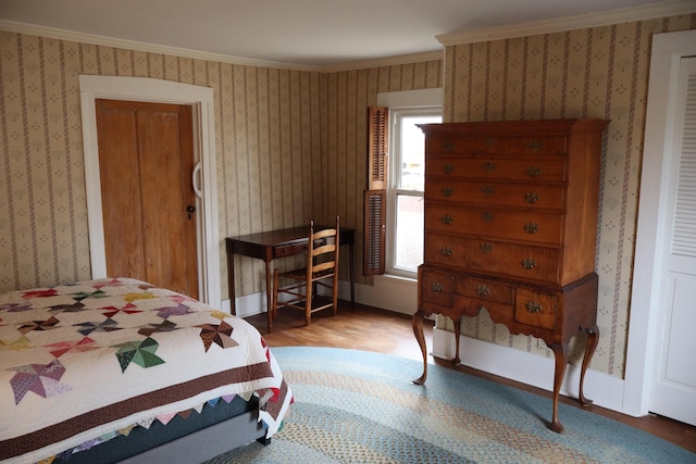 bedroom featuring baseboards, wood finished floors, ornamental molding, and wallpapered walls