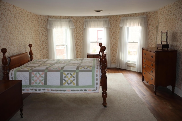 bedroom featuring visible vents, wallpapered walls, and wood finished floors