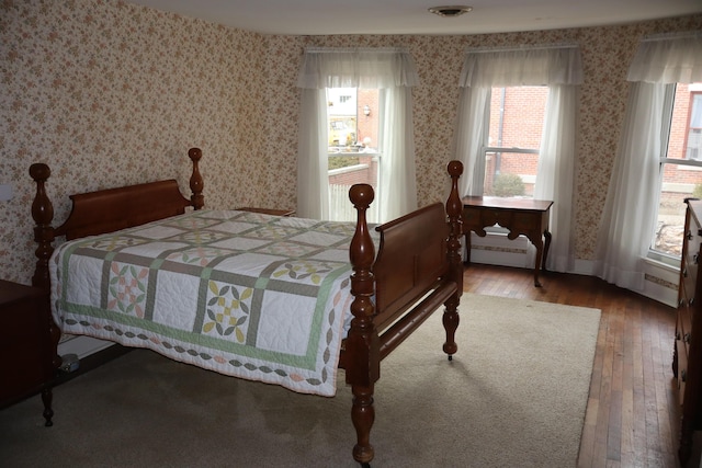 bedroom with wallpapered walls, baseboard heating, baseboards, and hardwood / wood-style floors