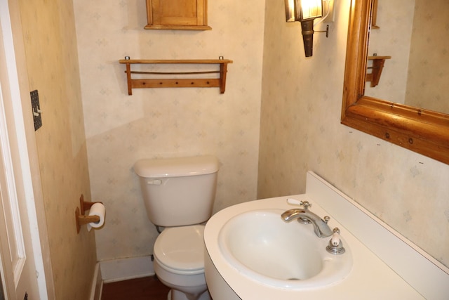 bathroom featuring wallpapered walls, toilet, baseboards, and a sink