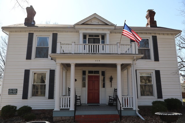 view of front facade featuring a balcony, covered porch, and a chimney