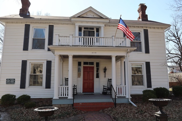 view of front of home with a balcony, covered porch, and a chimney