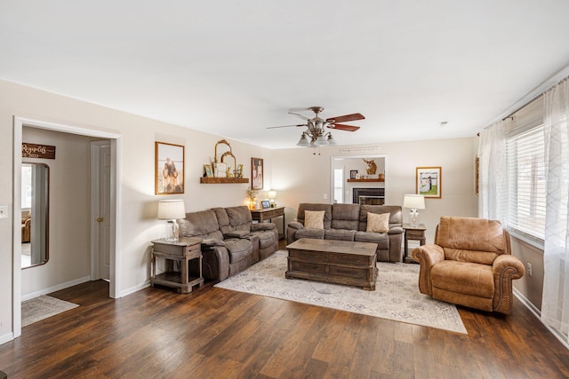 living room with ceiling fan, a fireplace, baseboards, and wood finished floors