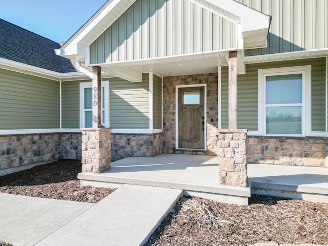 doorway to property featuring a porch, stone siding, board and batten siding, and a shingled roof