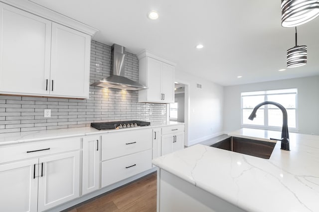 kitchen with light wood-type flooring, a sink, backsplash, stainless steel gas stovetop, and wall chimney exhaust hood