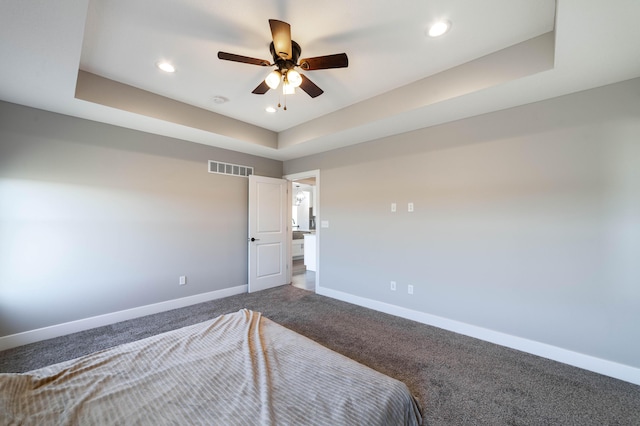 unfurnished bedroom with visible vents, baseboards, dark carpet, a tray ceiling, and recessed lighting