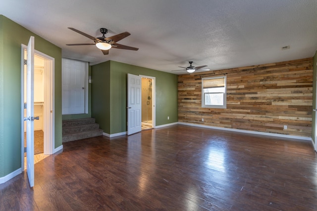 unfurnished room with a textured ceiling, wood finished floors, wood walls, baseboards, and stairs