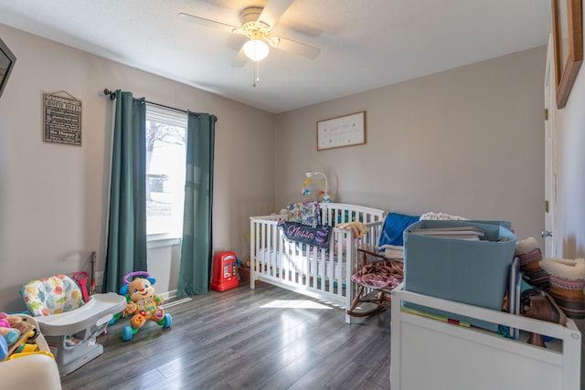 bedroom featuring ceiling fan, a crib, a textured ceiling, and wood finished floors