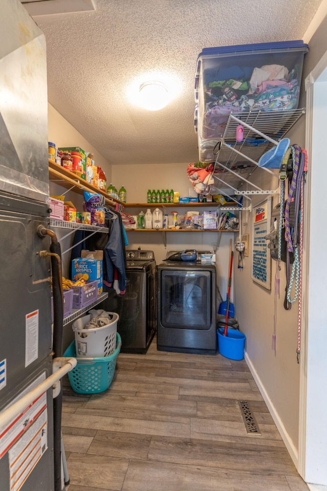 clothes washing area with wood finished floors, visible vents, laundry area, a textured ceiling, and washer and clothes dryer