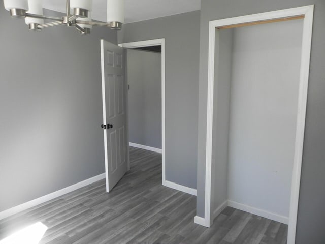 unfurnished bedroom with dark wood-style floors, a notable chandelier, and baseboards