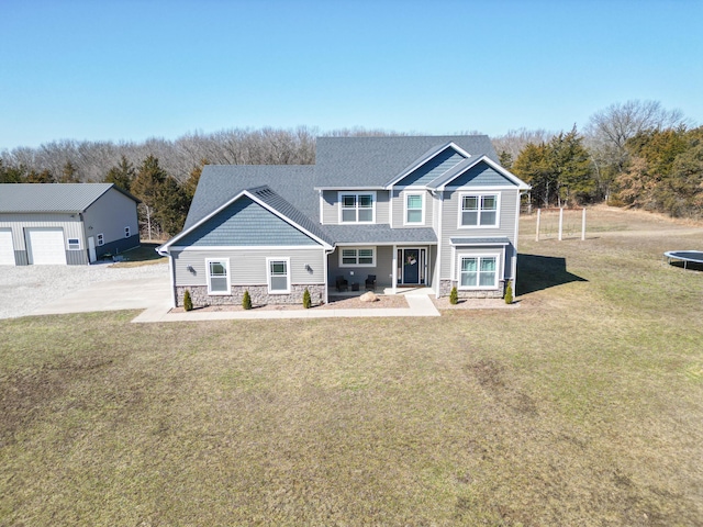 view of front of property with a trampoline, a front yard, stone siding, and a shingled roof