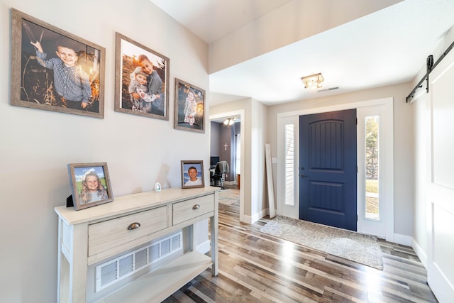 foyer featuring wood finished floors, visible vents, baseboards, and a barn door