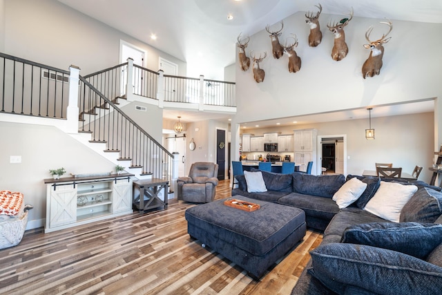 living room featuring light wood-style floors, stairs, baseboards, and a notable chandelier