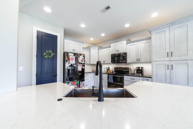 kitchen with a sink, visible vents, double oven range, black refrigerator with ice dispenser, and stainless steel microwave